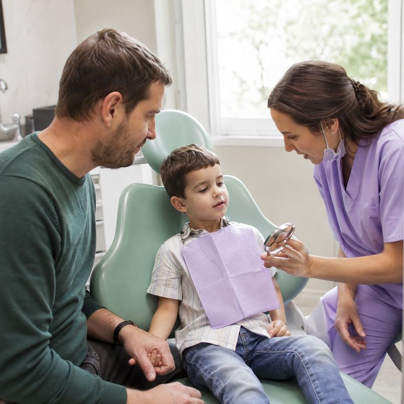 A young boy in a dental chair holding his father's hand